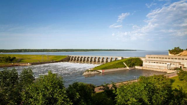 A dam with green landscape around it and a blue sky in the background